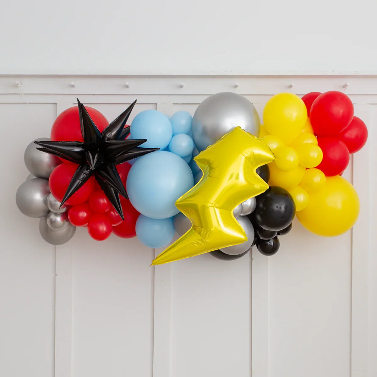 Colorful superhero party balloon garland with star and lightning foil balloons on white wall