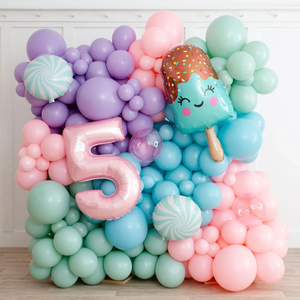 Colorful balloon wall with pastel mint, pink, purple, and blue balloons, featuring a pink number 5 and an ice cream balloon