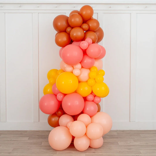 Tropical sunset balloon pillar in warm shades of orange, pink, and yellow on wood floor