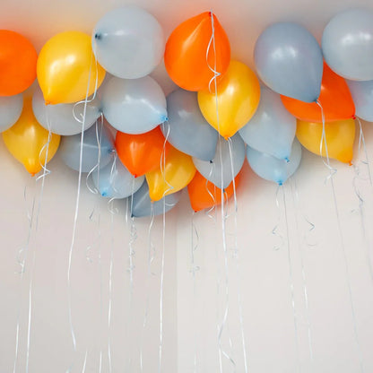 Cluster of orange, yellow, and grey helium balloons floating against white ceiling