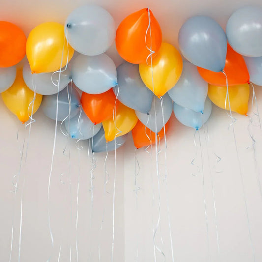 Cluster of orange, yellow, and grey helium balloons floating against white ceiling
