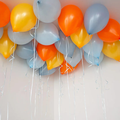 Cluster of helium balloons in orange, yellow, and gray colors floating on a ceiling with curling ribbons