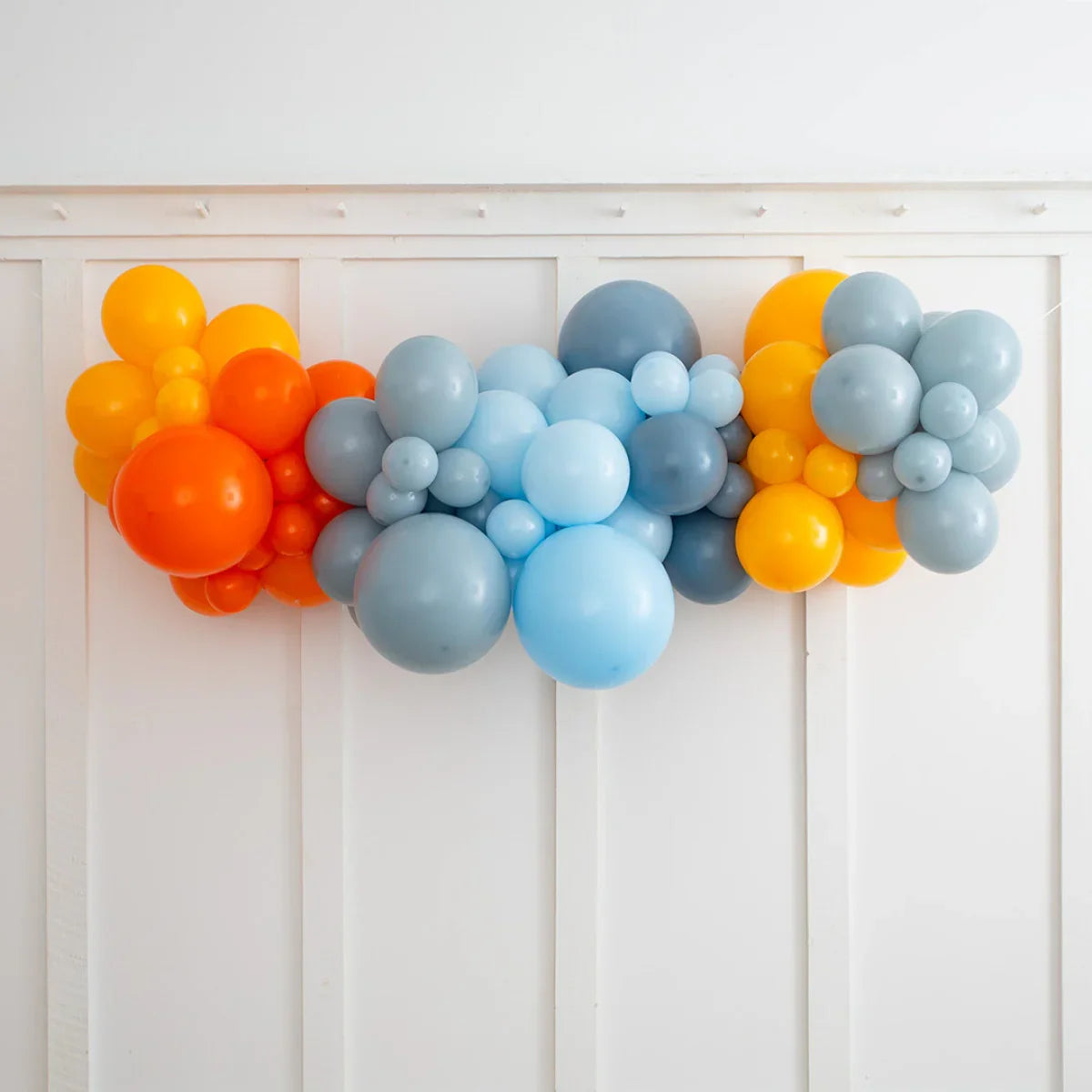 Colorful balloon garland decoration with orange, yellow, blue, and gray balloons on white wall