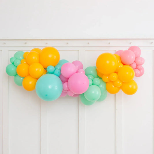 Colorful inflated balloon garland in orange, pink, and teal hanging on a white paneled wall