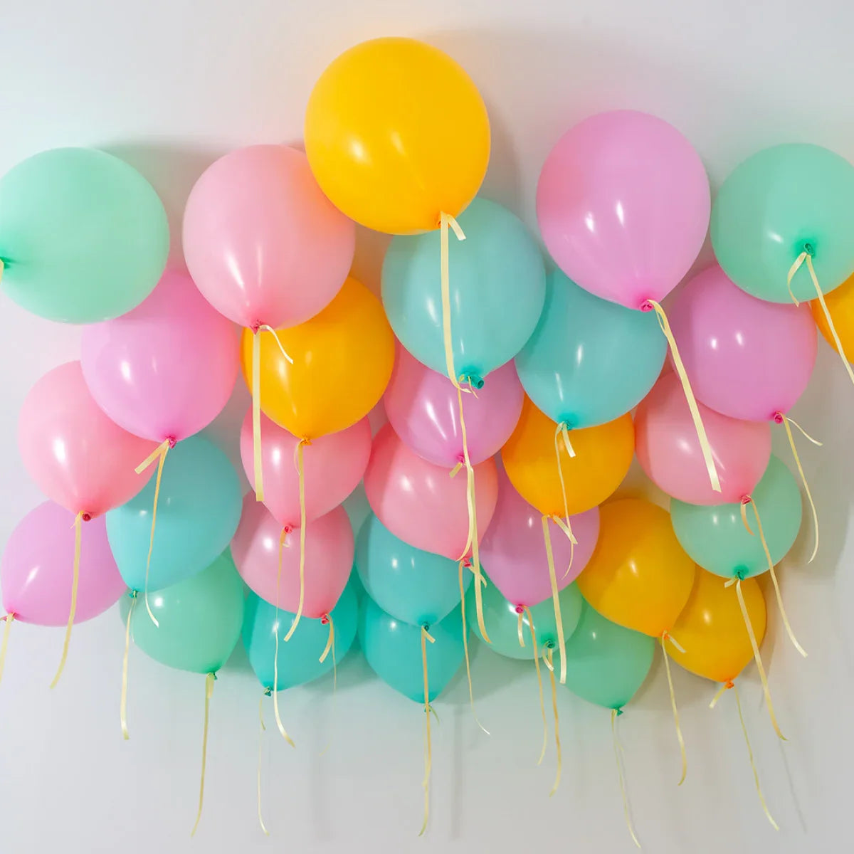 helium balloons in pastel pink, yellow, and teal colors attached to ceiling for party decoration