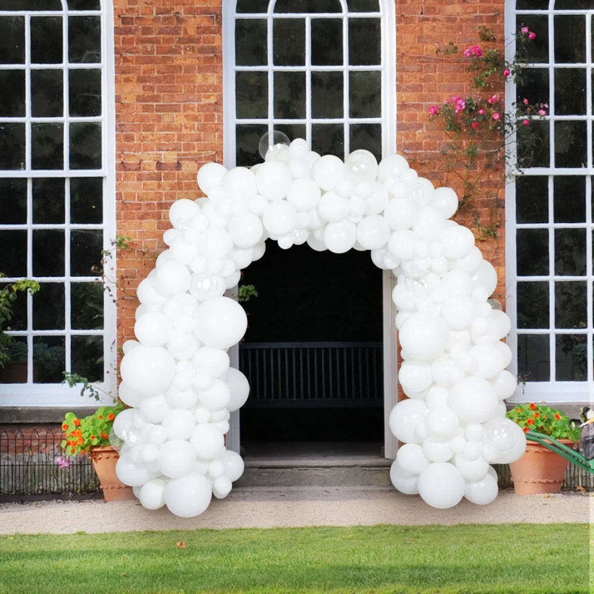White balloon arch decoration at outdoor wedding venue with brick wall and large windows