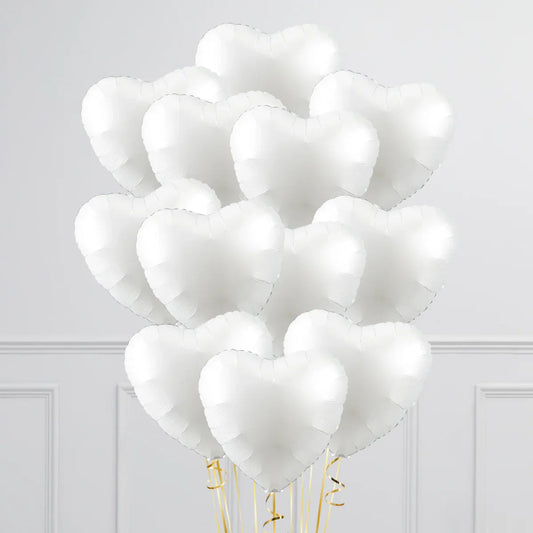 Bunch of white heart-shaped inflated foil balloons with gold ribbons against a light gray wall