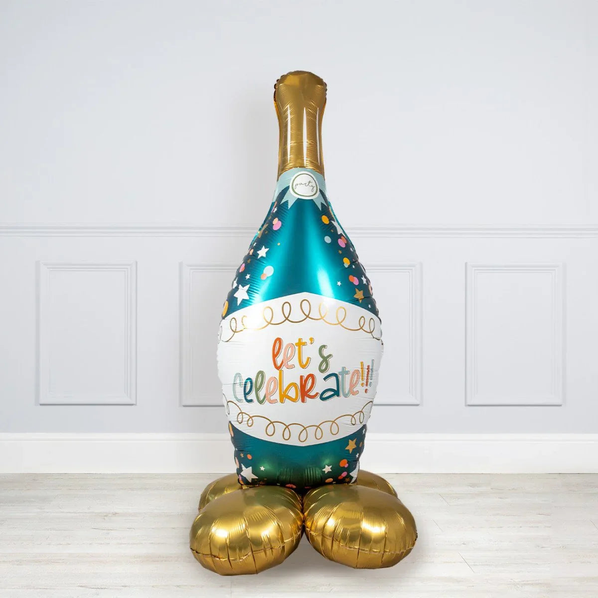 Large foil balloon shaped like a champagne bottle with colorful confetti and text 'let's celebrate' on white wall background