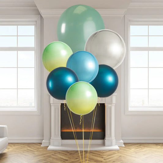 Colorful helium balloons in blue, green, and silver inside a bright room with white fireplace and windows