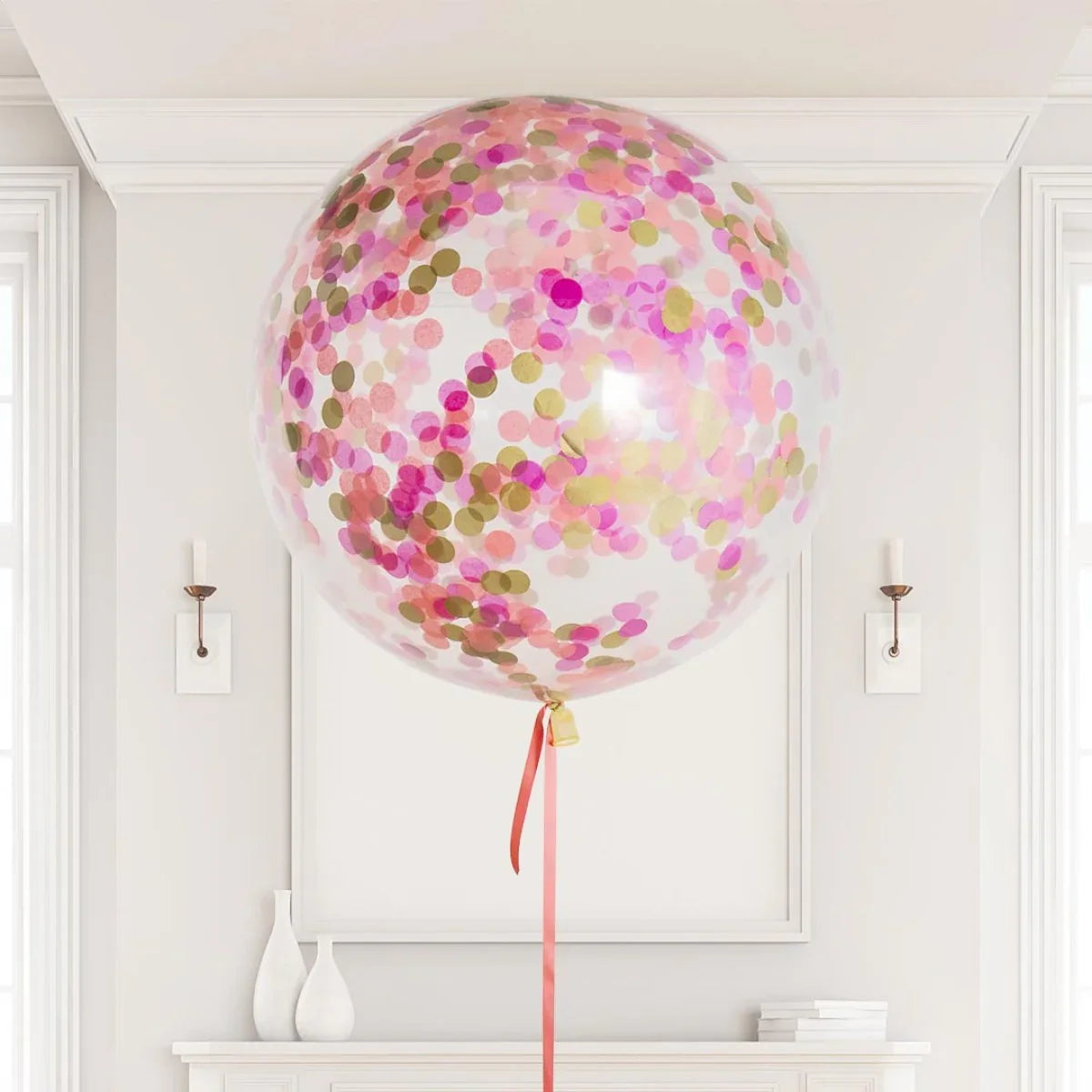 Large transparent balloon filled with pink and gold confetti floating indoors above white mantel