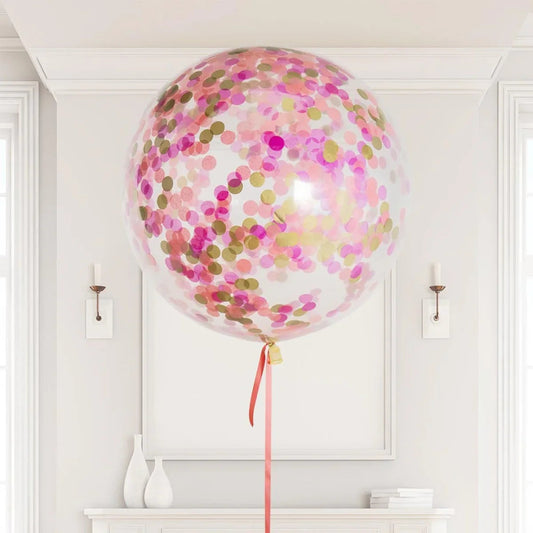 Large transparent balloon filled with pink and gold confetti floating indoors above white mantel