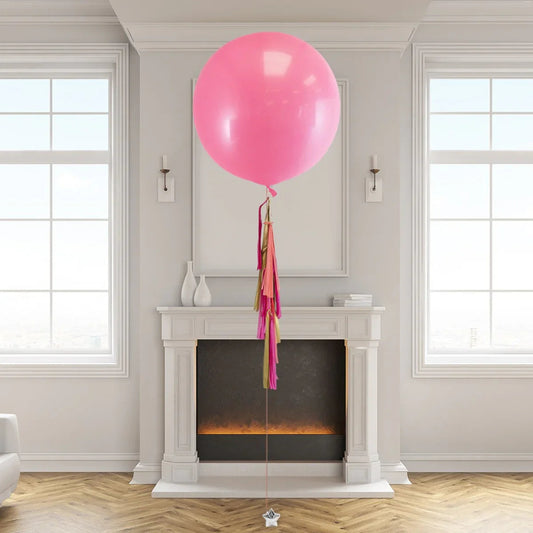 Giant pink helium balloon with pink and gold tassel tail floating in elegant living room