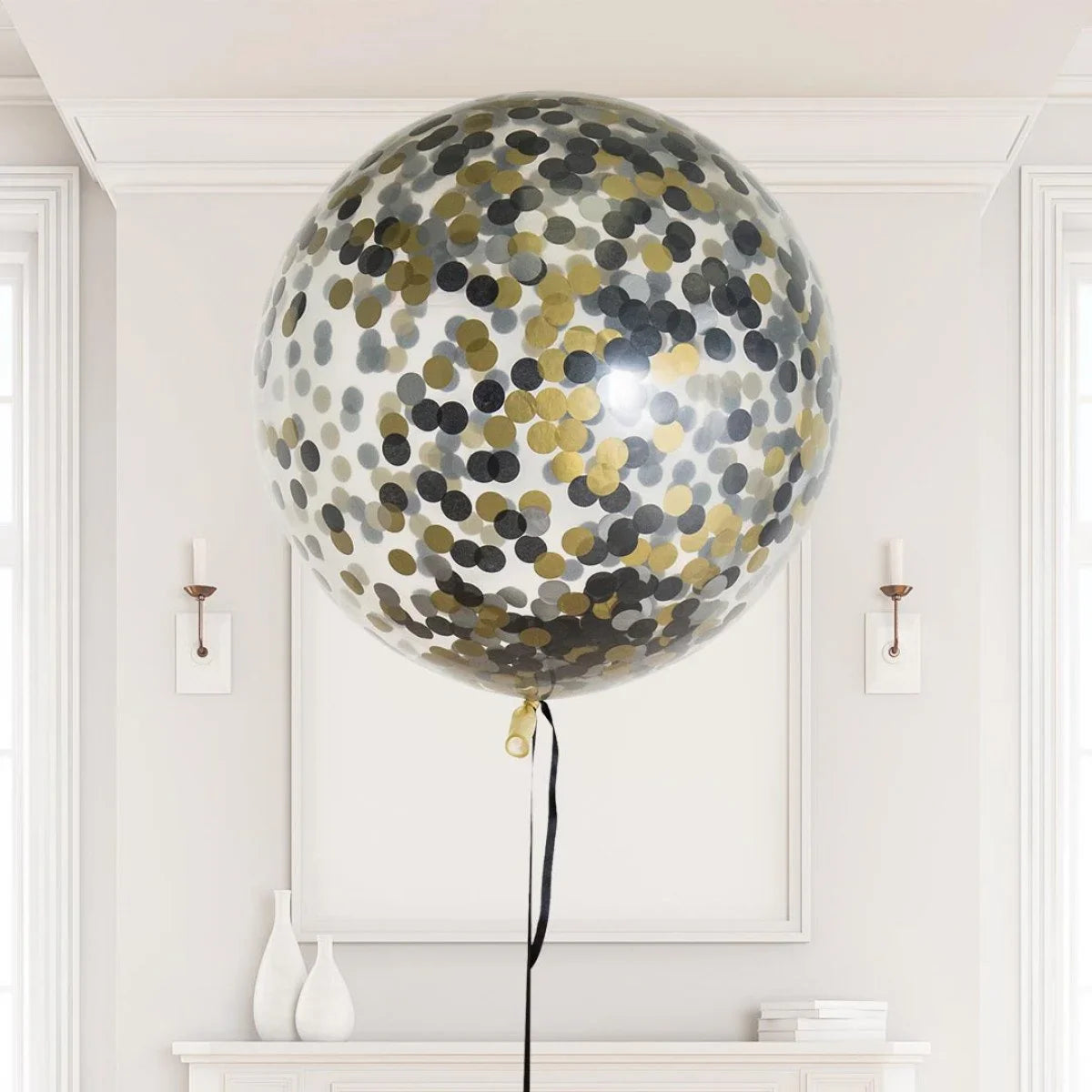 Giant clear helium balloon filled with gold and black confetti floating in elegant white room