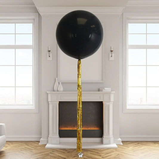 Giant black balloon with gold foil tassel in elegant living room with fireplace and large windows