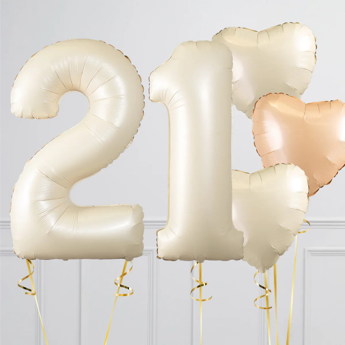 Champagne gold foil balloons shaped as number 21 and heart balloons with gold ribbons on white background