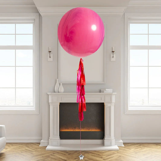 Large pink helium balloon with red tassels tied by white fireplace in modern living room