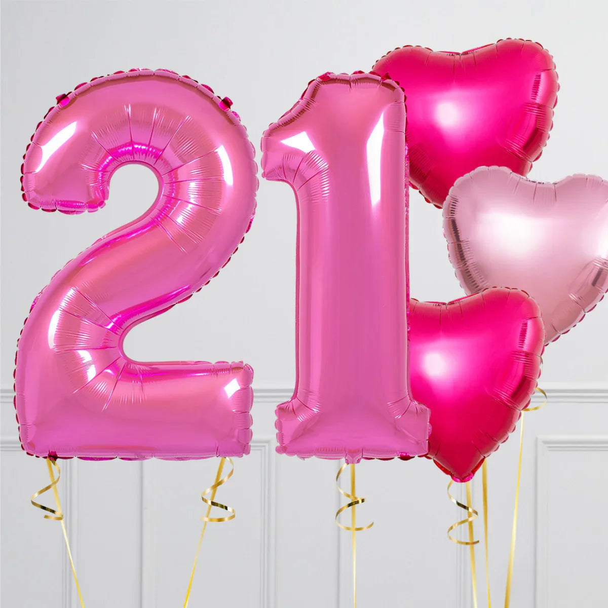 Pink foil balloons shaped as number 21 and heart shapes against a white paneled wall