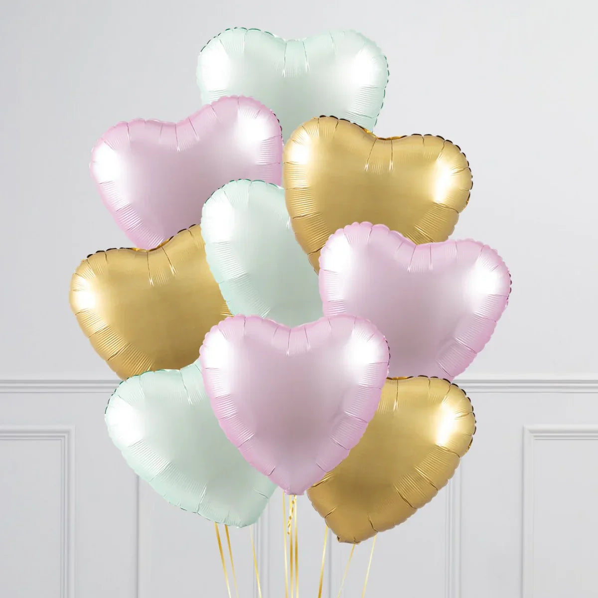 Cluster of metallic heart-shaped balloons in pastel pink, gold, and mint green against white wall