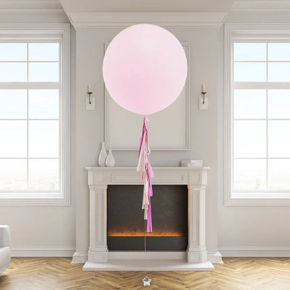 Large pastel pink balloon with pink and white tassels floating in elegant room with mantle and windows