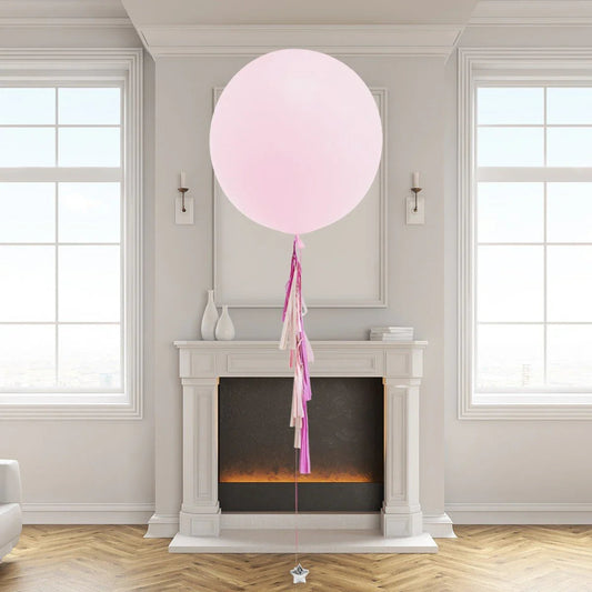 Large pastel pink balloon with pink and white tassels floating in elegant room with mantle and windows