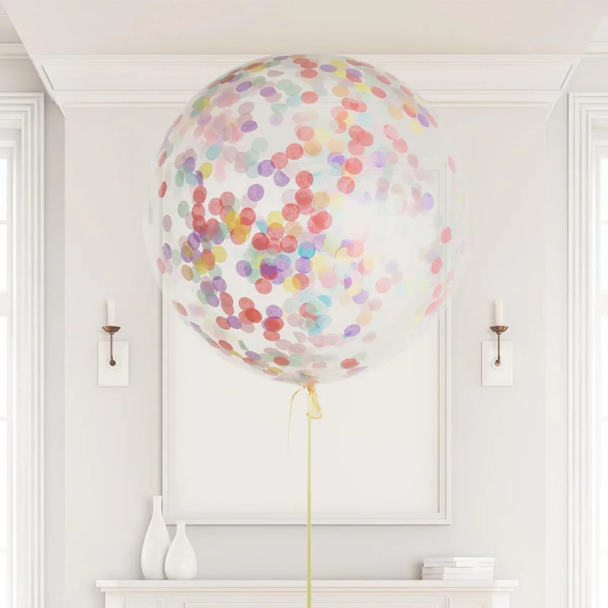 Large clear balloon filled with multicolored confetti floating indoors above white mantel