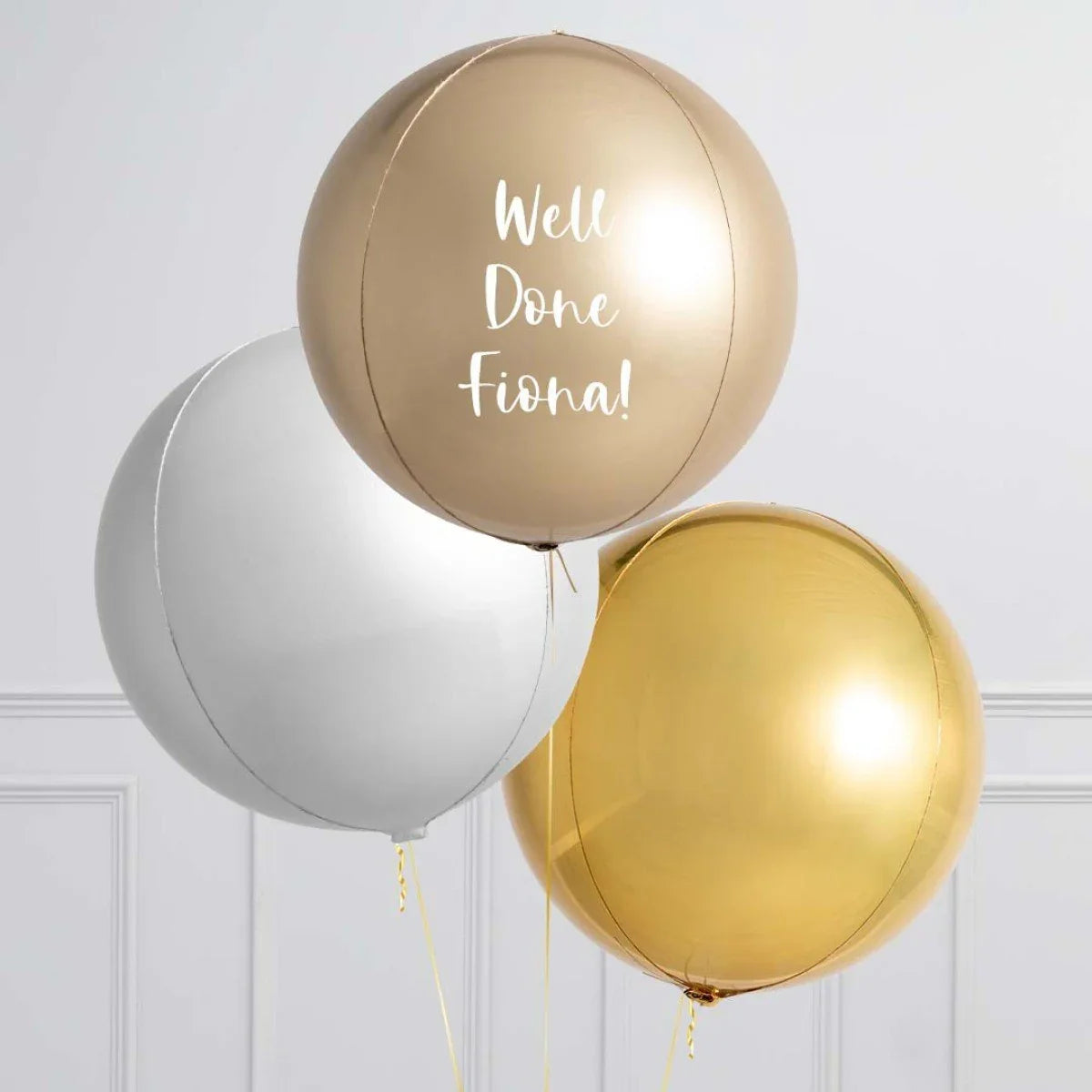 Three large metallic balloons in champagne, silver, and gold with champagne balloon saying 'Well Done Fiona'