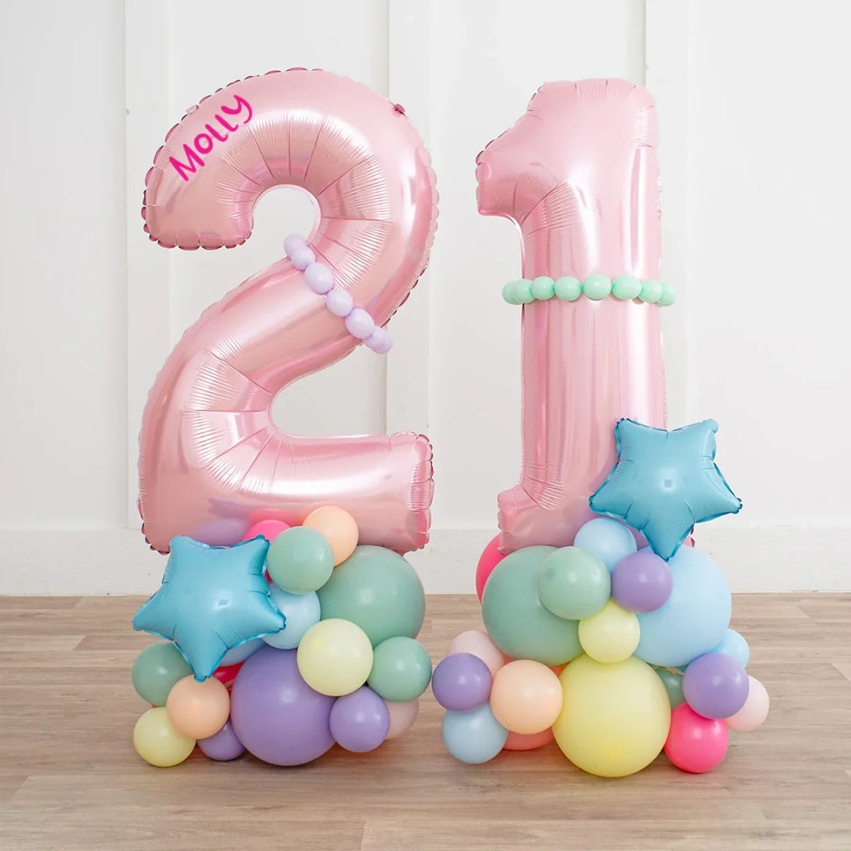 Pink foil balloons shaped as numbers 2 and 1 with pastel multicolor balloon clusters and blue star balloon