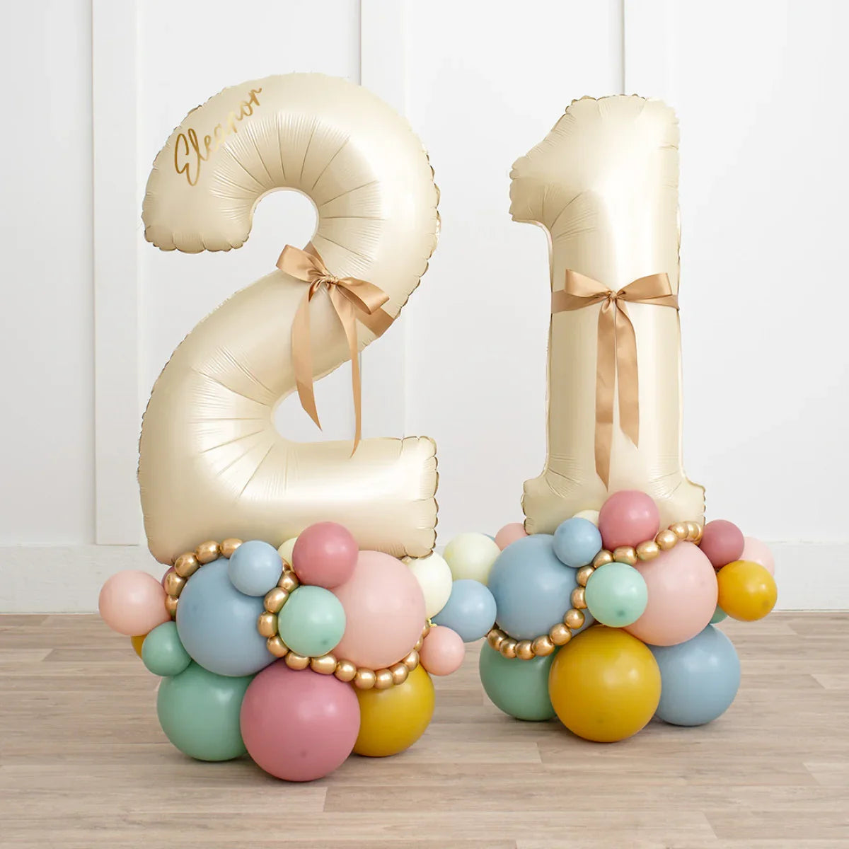 Gold number 21 balloons with satin bows and pastel multicolor balloon base on wooden floor