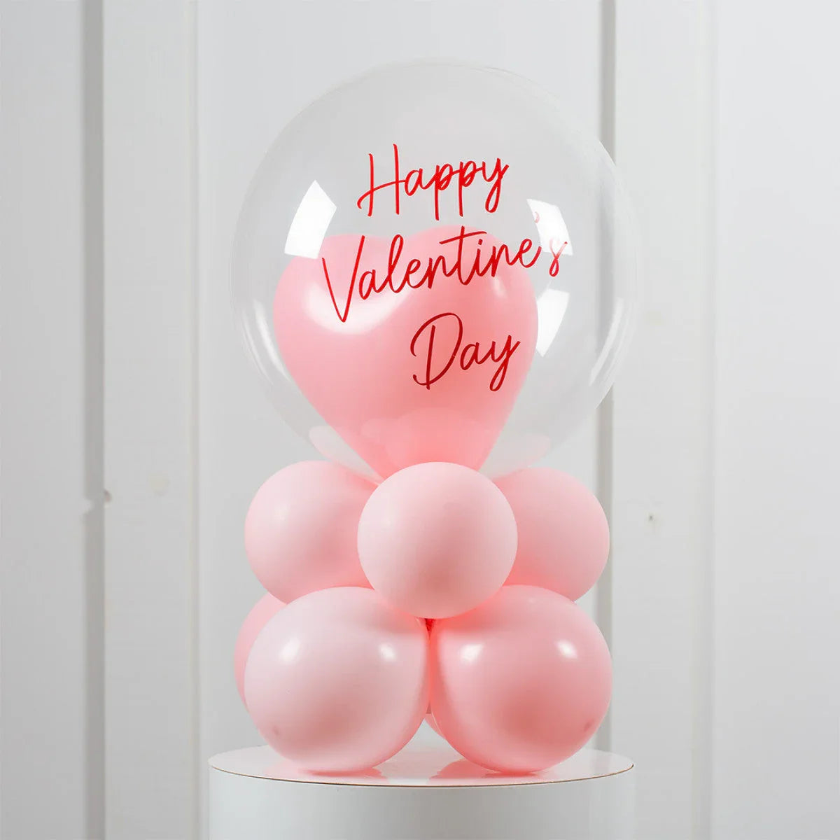 Valentine's Day balloon arrangement with pink heart and bubble balloons on white pedestal