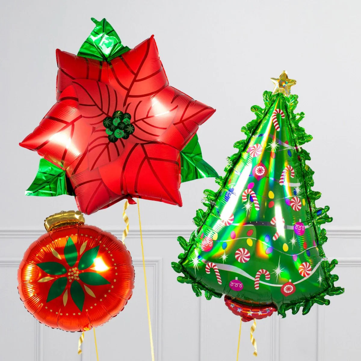 Christmas balloons featuring red poinsettia, green decorated Christmas tree, and red ornament against white wall