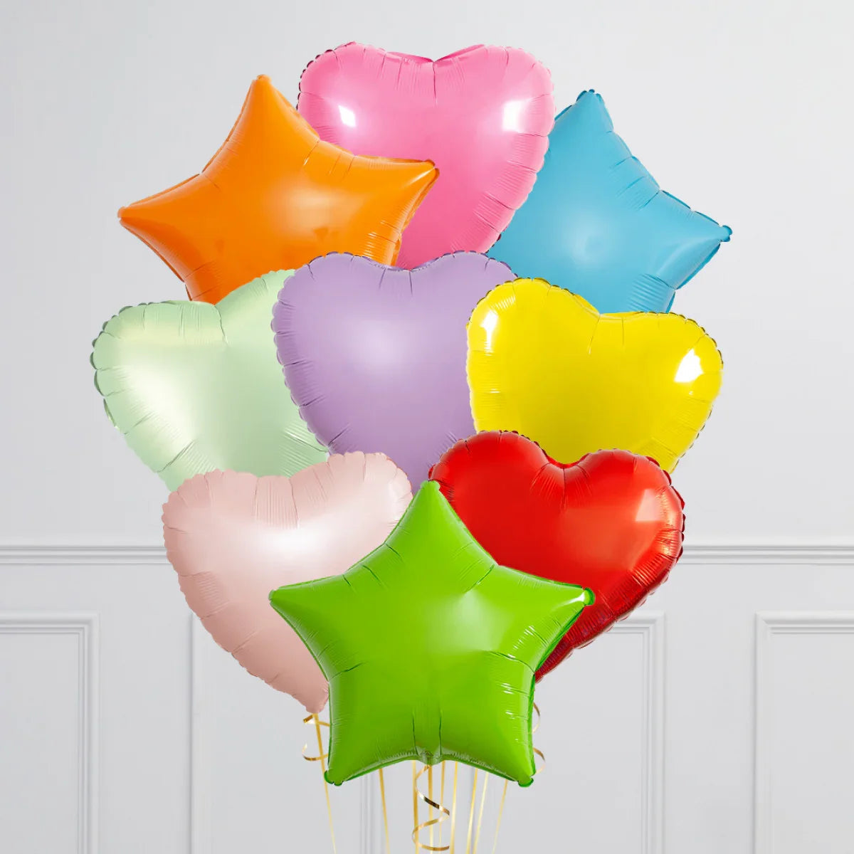 Bright heart and star-shaped balloons in pastel and vibrant colors against white wall