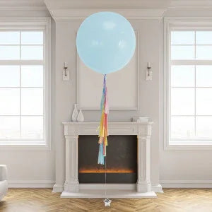 Large light blue helium balloon with rainbow tassel tail floating in a modern living room above a white fireplace