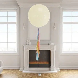 Large cream helium balloon with colorful tassel tail floating in elegant living room above fireplace