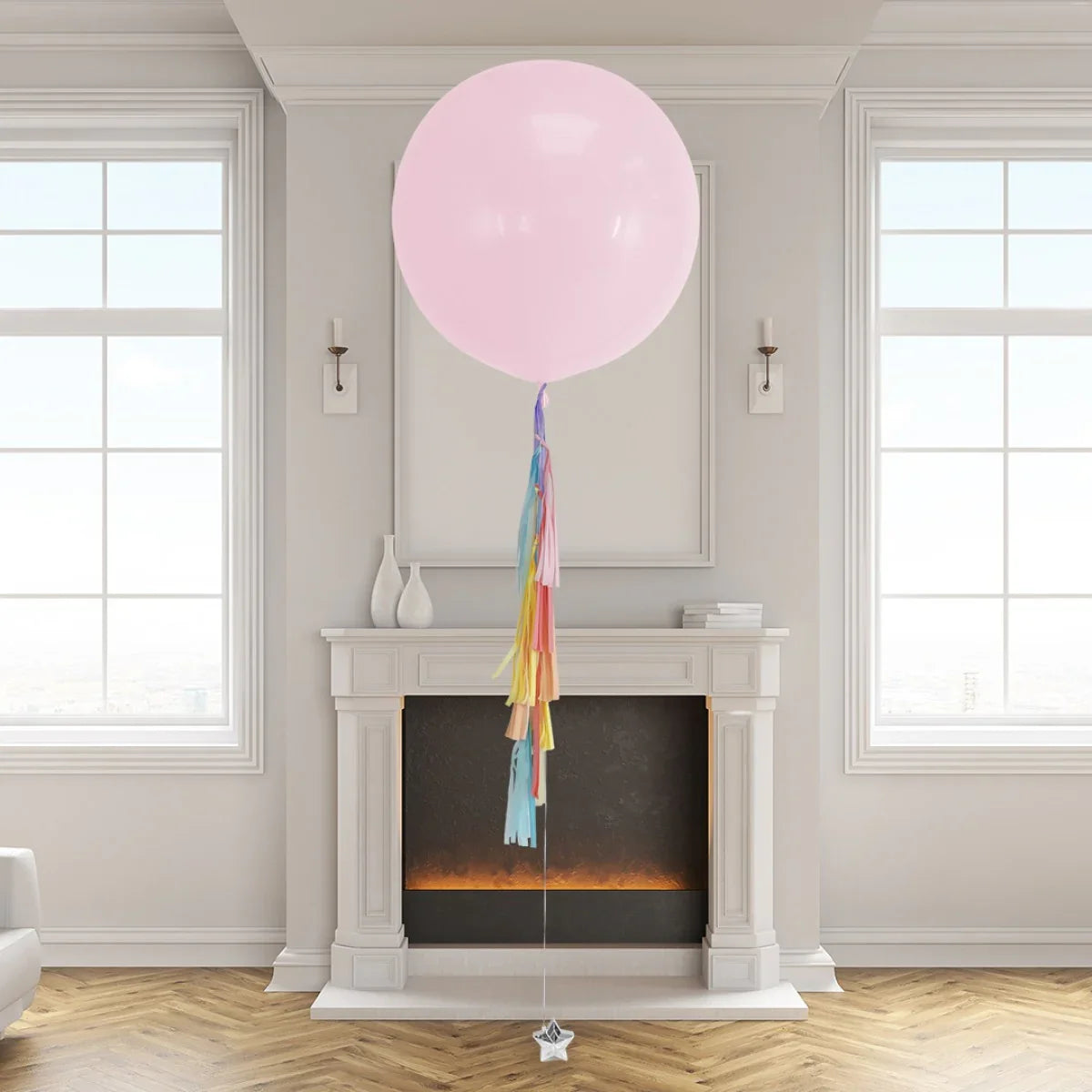Large pink helium balloon with rainbow tassel tail floating in modern living room near white fireplace