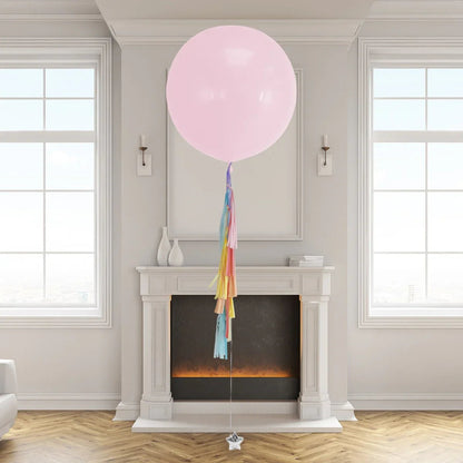 Large pink helium balloon with rainbow tassel tail floating in modern living room near white fireplace