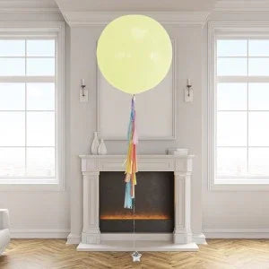 Large yellow helium balloon with rainbow tassel tail in elegant room with fireplace and tall windows