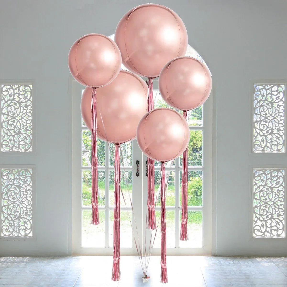 Giant rose gold orb balloons with matching tassels in bright room near white glass doors