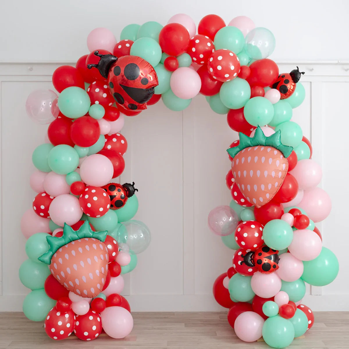 Colorful balloon arch with red, pink, mint green balloons, strawberry and ladybug foil balloons indoors