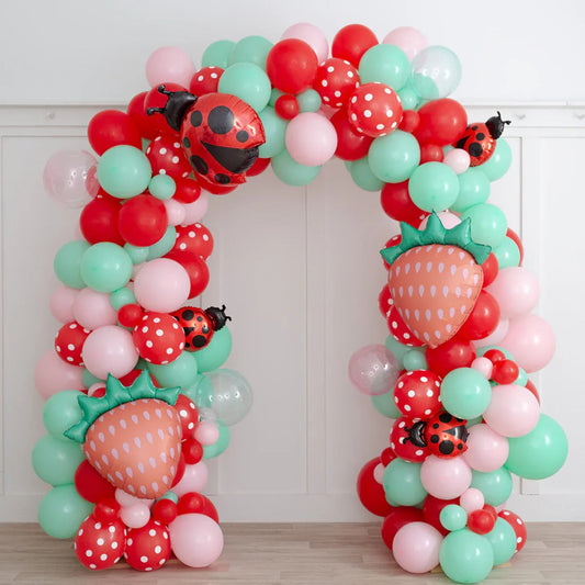 Colorful balloon arch with red, pink, mint green balloons, strawberry and ladybug foil balloons indoors