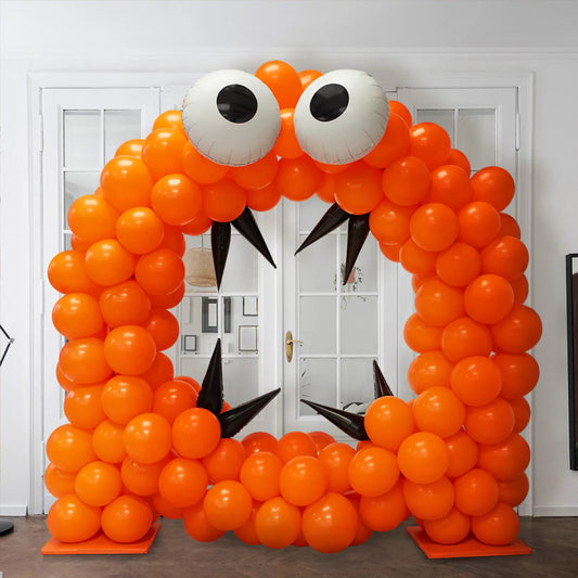 Orange balloon arch shaped like a monster face with big eyes and black spike fangs indoors