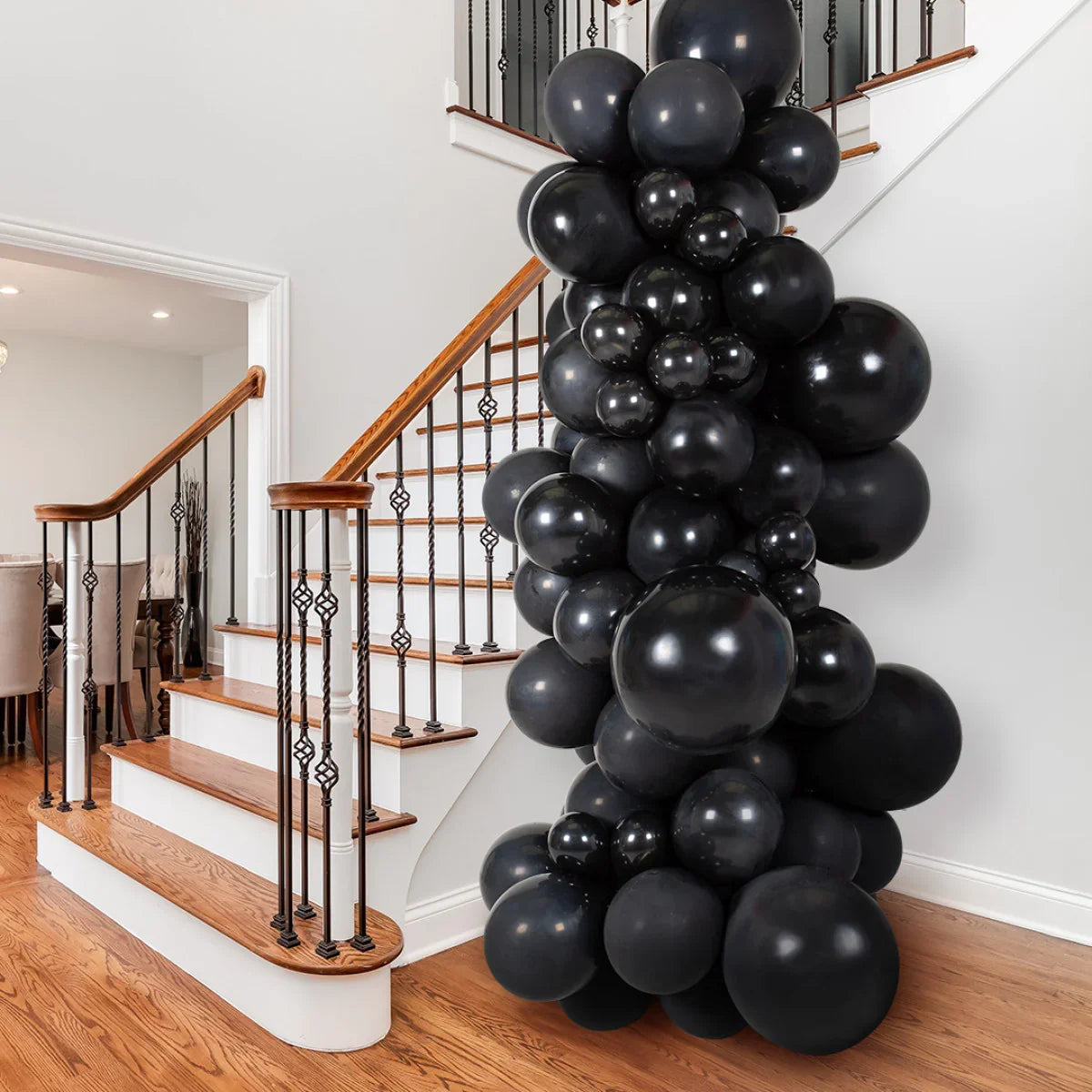 Tall black balloon garland decoration displayed on wooden staircase with white walls and iron railings