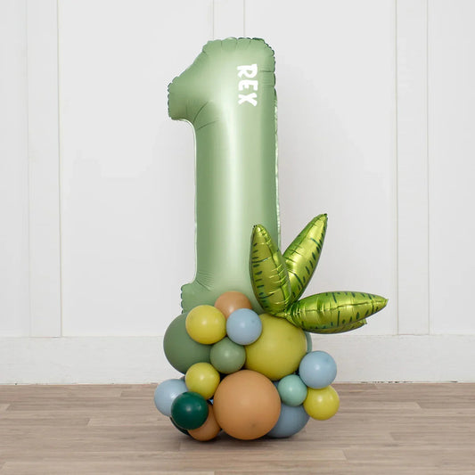 Green number 1 balloon with text REX and multicolor cluster balloons on wooden floor