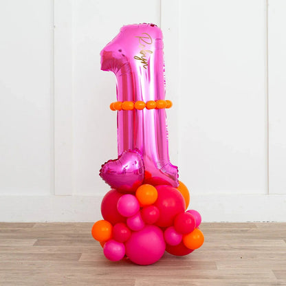 Pink foil balloon shaped as number 1 with orange and pink round balloons decoration on wood floor against white wall