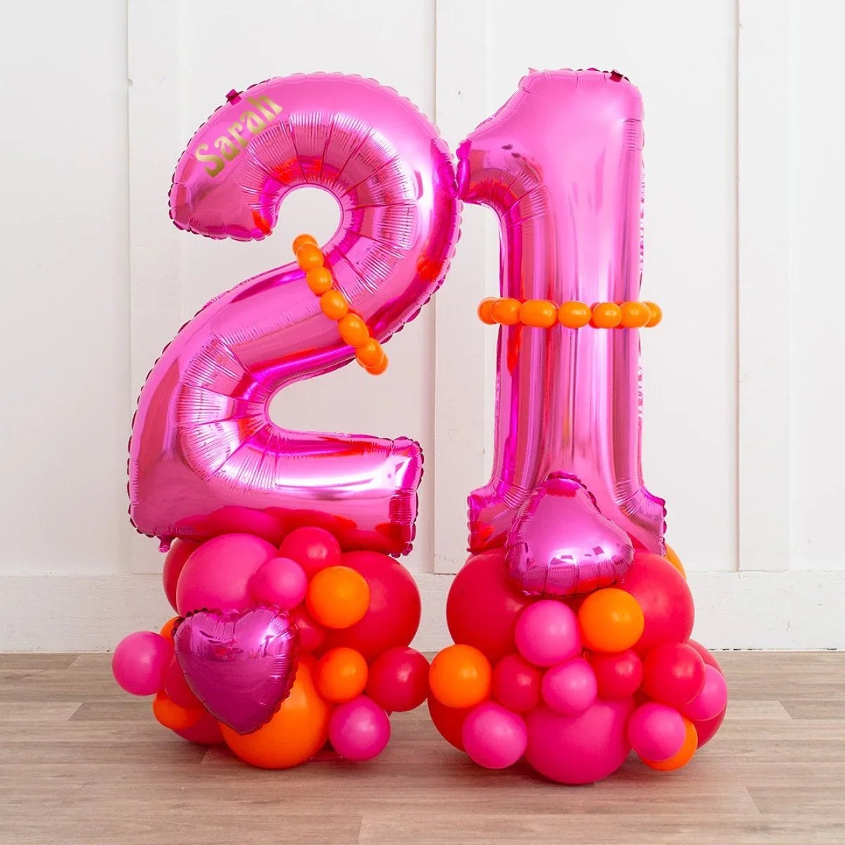 Pink metallic number 21 balloons decorated with orange and pink small balloons on wooden floor