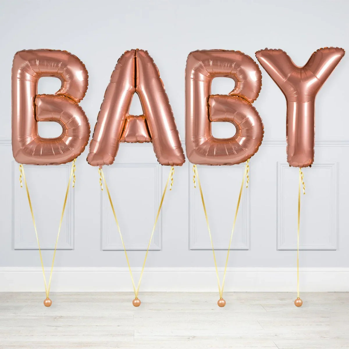 Rose gold helium balloons spelling the word BABY, tied with gold ribbons indoors