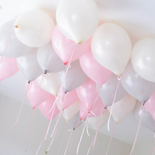 Cluster of pink, white, and silver helium balloons floating against a white ceiling with ribbons