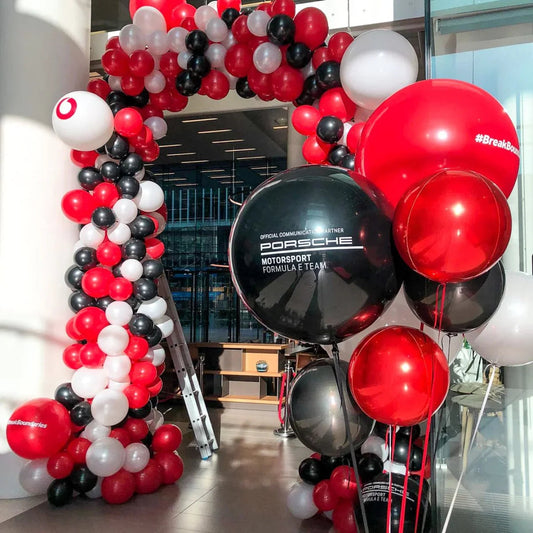 Red, black, and white balloons arch and cluster decorating an indoor space, featuring Porsche Motorsport Formula E logos
