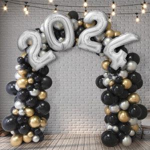 2024 silver number balloon arch with black, gold, and white balloons against white brick wall
