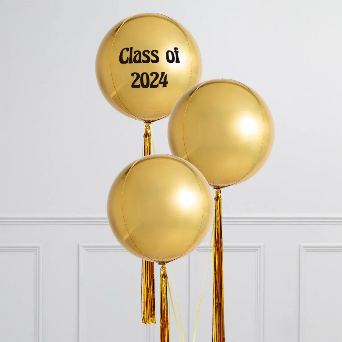 Three large shiny gold balloons with tassels, one balloon reads Class of 2024