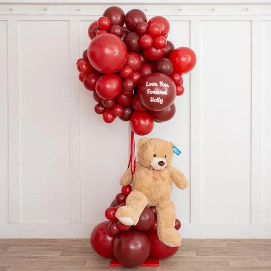 Red and burgundy balloon bouquet with a teddy bear and message balloon saying Love You Forever Holly